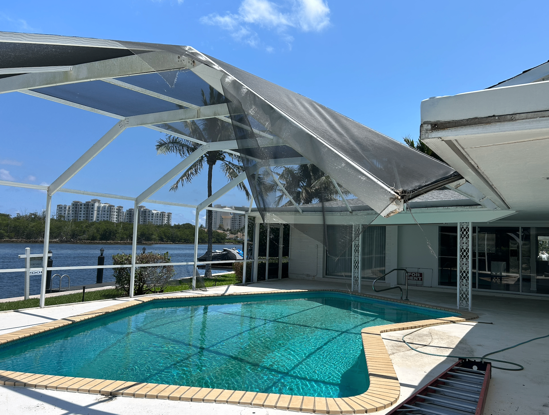 Storm-damaged pool enclosure and lanai screen collapsed over a swimming pool in South Florida