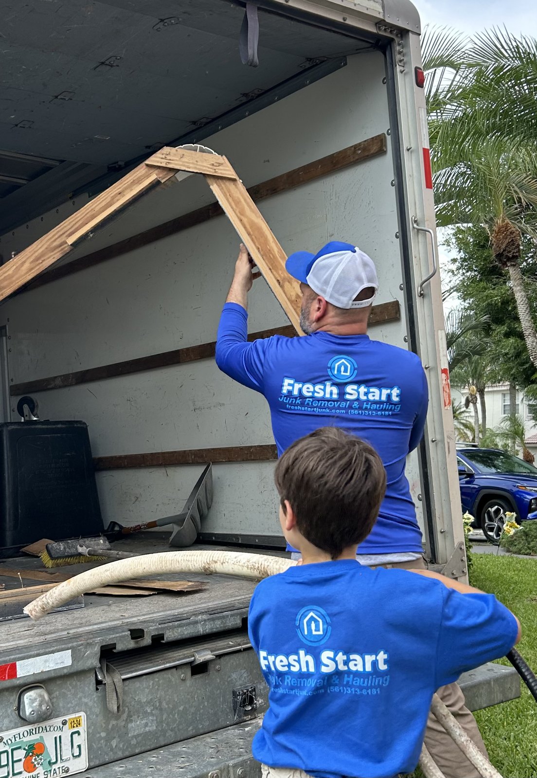 Owner of Fresh Start Junk Removal & Hauling and his son loading a wood frame into the branded truck during a South Florida junk removal job
