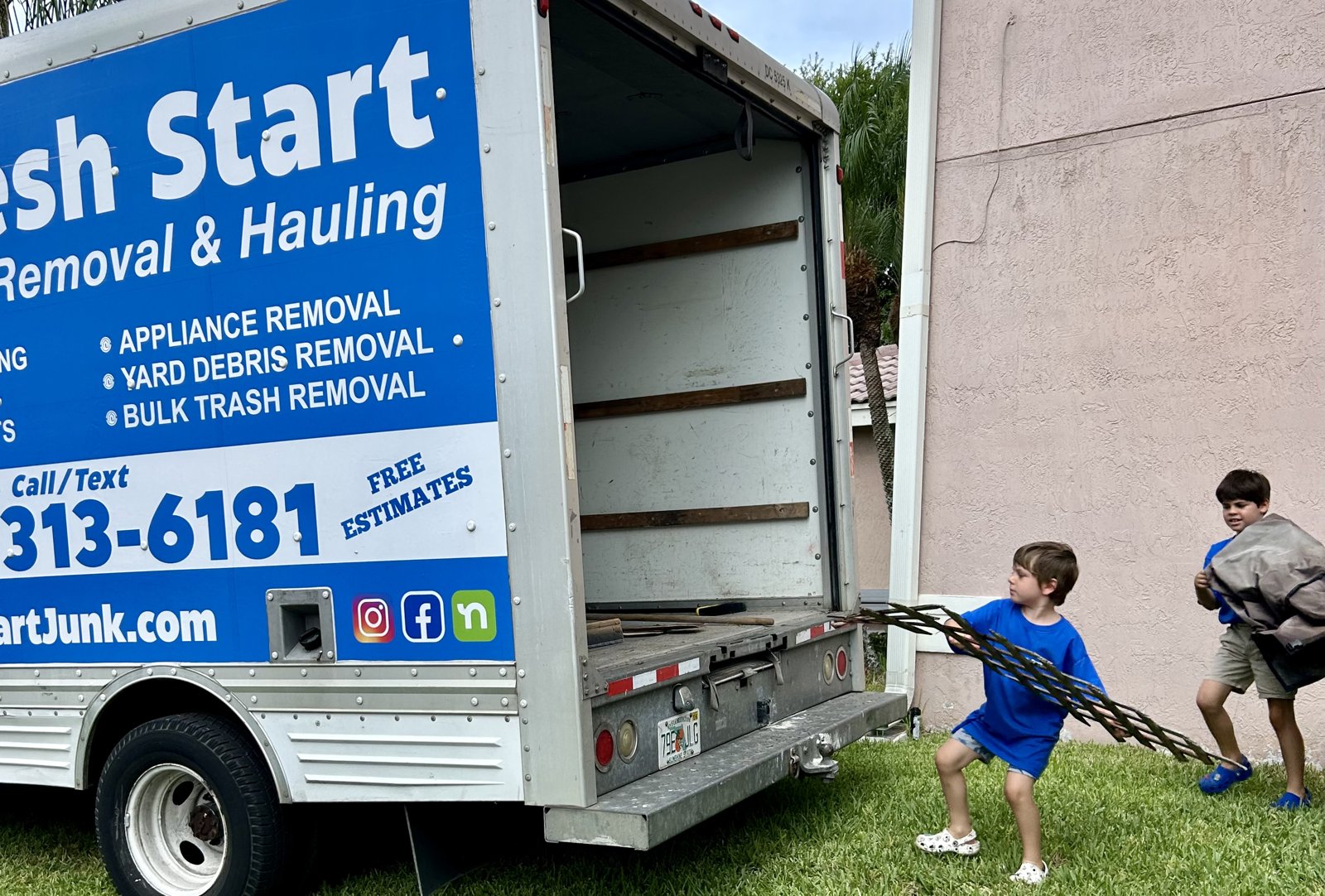 Fresh Start Junk Removal crew. The owner's kids in branded shirts hauling palm-frond yard debris to the truck in Boca Raton, Florida
