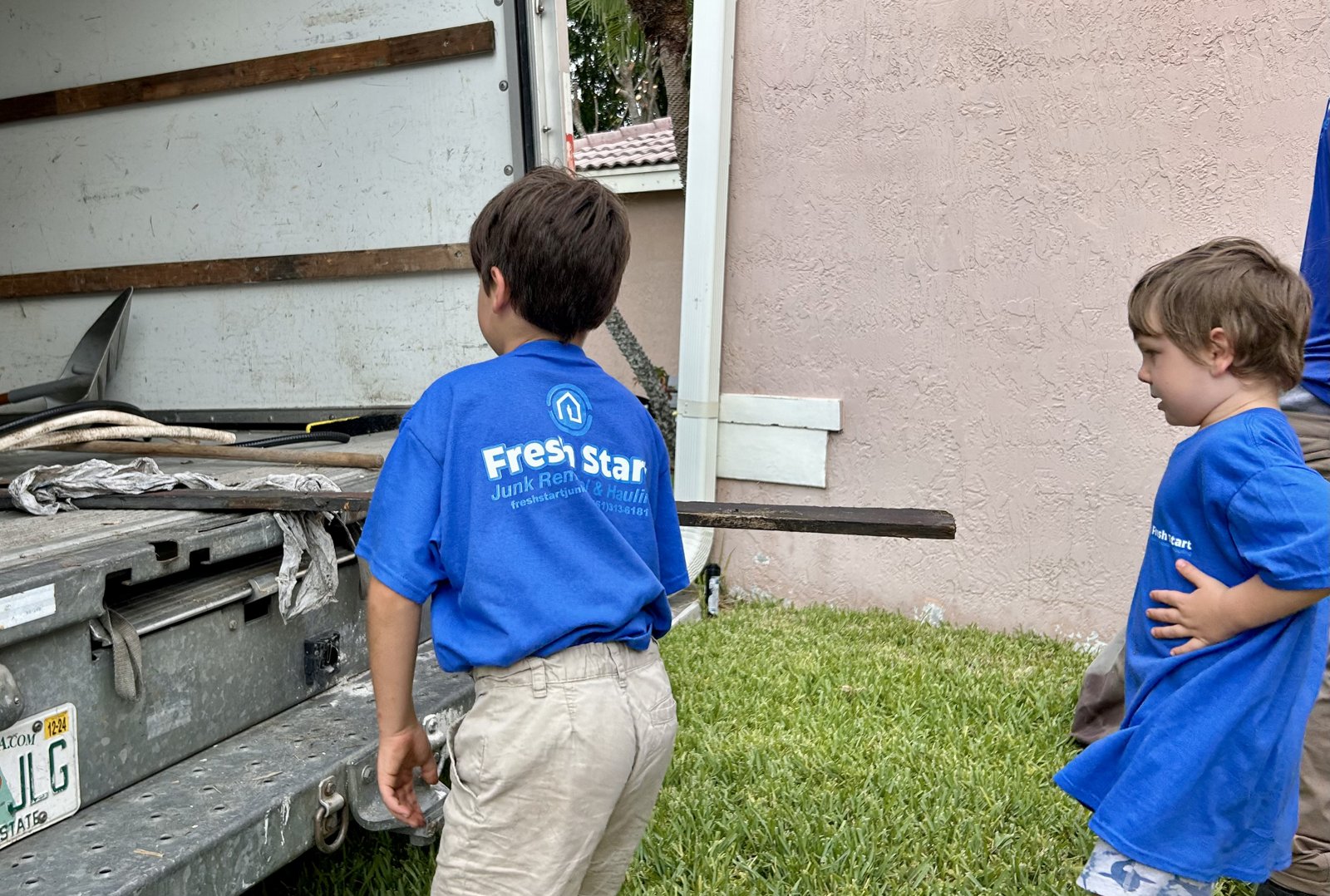 Fresh Start Junk Removal. Kids in branded shirts loading debris at the back of the family-owned junk removal truck in South Florida